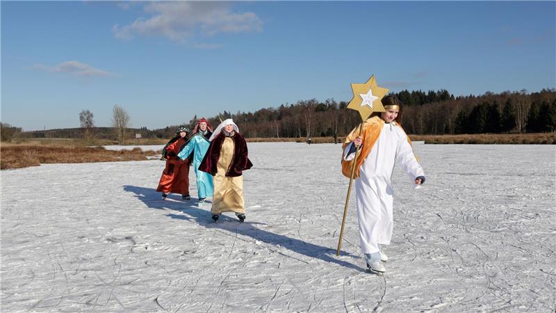 Sternsinger sind im Sonnenschein bei Betzenweiler in Tiefenbach mit Schlittschuhen auf einem zugefrorenen See unterwegs. 