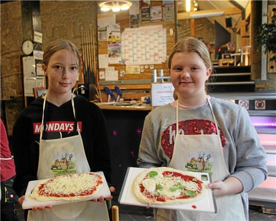 Stolz präsentieren die Mädchen ihre selbstgemachten Pizzen: Der Teig wird von ihnen ausgerollt und in Form gebracht. Die Zutaten können sie sich ebenfalls selbst aussuchen. Jetzt muss sie nur noch in den Pizzaofen geschoben werden Rundes Bild: Auch auf dem Grill mit Pizzastein bekommen die Pizza eine schöne Farbe. Foto: Jenzora