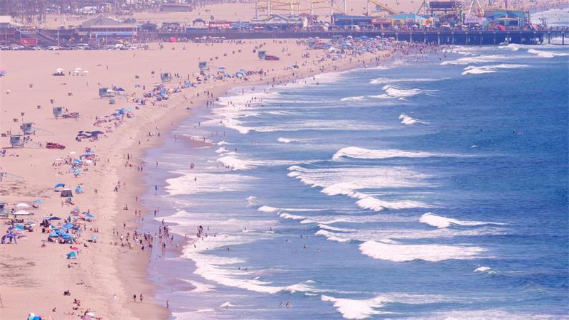 Strandbesucher halten sich am Santa Monica State Beach auf, während im Hintergrund der Santa Monica Pier zu erkennen ist.