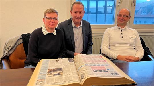 Eine Frau und zwei Männer sitzen zusammen und schauen in die Kamera.