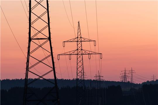 Strommasten sind bei Sonnenaufgang als Silhouette zu sehen.