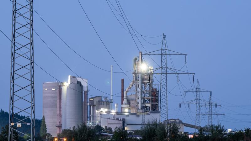 Kabinett will CO2-Speicherung in Deutschland möglich machen Strommasten stehen im Morgenlicht vor einem Zementwerk.