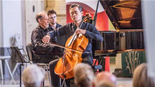 Sung-Won Yang (Cello) und Enrico Pace (Klavier) spielen in St. Stephani. Im Hintergrund James Solice vom Team des Internationalen Musikfests, der die Notenhefte umblättert.