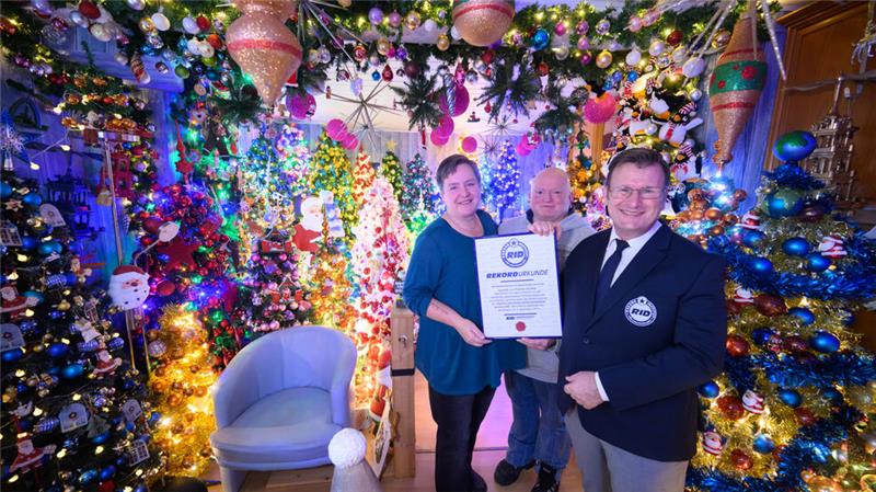 Susanne und Thomas Jeromin stehen mit Olaf Kuchenbecker (r.) vom Rekord-Institut für Deutschland inmitten von Weihnachtsbäumen in ihrem Haus im Landkreis Schaumburg.