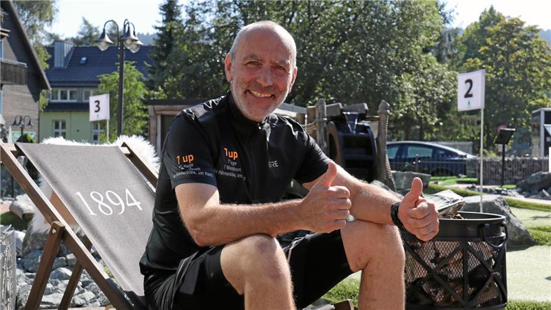Mann in schwarzem T-Shirt sitzt auf Liegestuhl mit der Zahl '1894' und zeigt beide Daumen nach oben