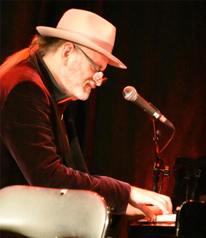 Ein Mann mit Hut sitzt am Klavier vorm Mikrofon.