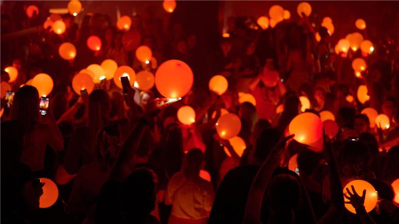 „Swifties“ erleuchten in Bochum auf einer Party der Reihe „Taylor Party Europe“ orangefarbene Luftballons mit den Lichtern ihrer Smartphones.
