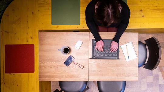 Symbolfoto: Eine Frau sitzt im Homeoffice am Küchentisch und arbeitet an einem Laptop.