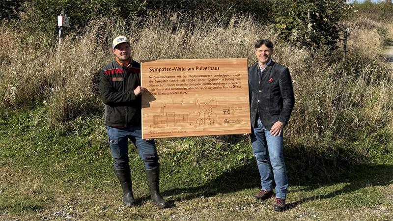 Zwei Leute halten ein Holzschild in der Natur.