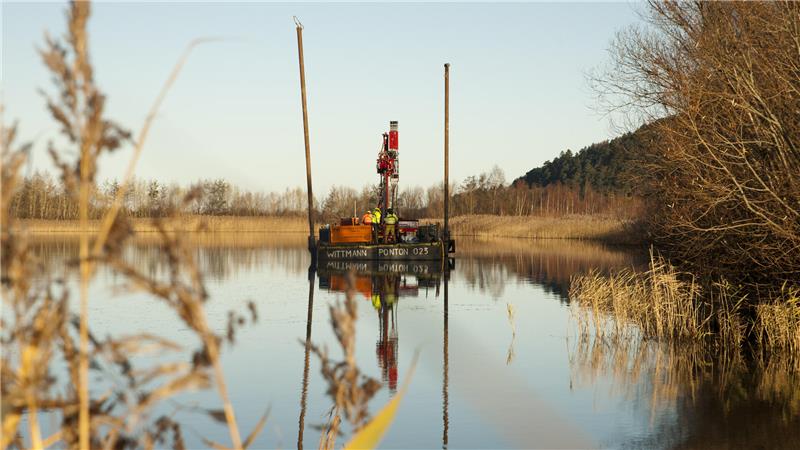 Mit einem Bagger auf einem schwimmenden Ponto holen Forscher Proben aus dem Schlamm des Bergeteichs.
