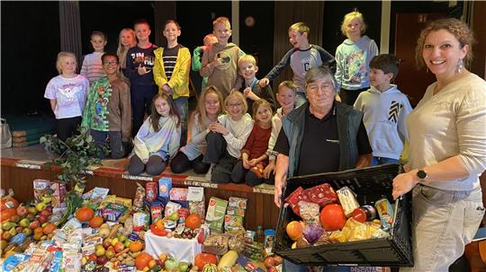 Tafel-Mitarbeiterin Edeltraud Breeger nimmt die Erntedank-Spenden von Lehrerin Julia Krüger-Köthe (re.) und der Klasse 3b entgegen.