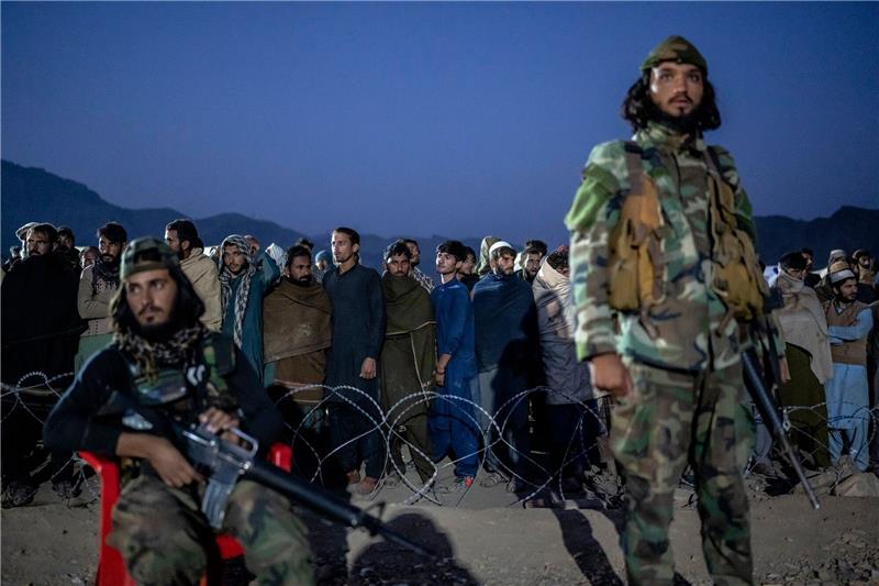 Mehr als 200.000 Afghanen haben Pakistan verlassen Taliban-Kämpfer stehen Wache, während afghanische Flüchtlinge in einem Lager nahe der pakistanisch-afghanischen Grenze anstehen, um sich registrieren zu lassen.