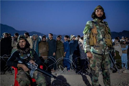 Taliban-Kämpfer stehen Wache, während afghanische Flüchtlinge in einem Lager nahe der pakistanisch-afghanischen Grenze anstehen, um sich registrieren zu lassen.