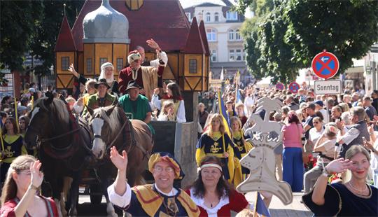 Ein Festumzug mit historischem Motivwagen schlängelt sich durch Besuchermassen.