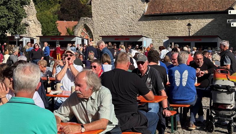 Das Foto zeigt viele Menschen, die an Tischen auf Bänken sitzen.