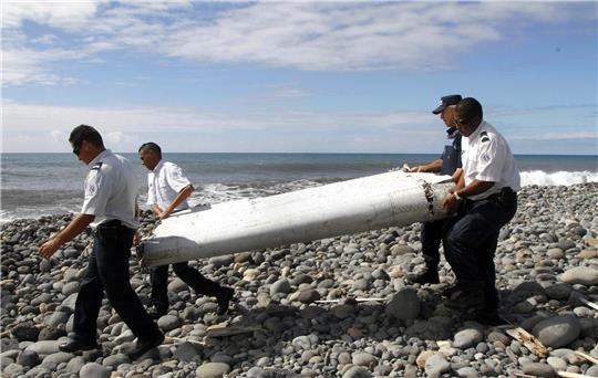 Techniker tragen ein Wrackteil, die Flügelklappe eines Flugzeugs, über einen Strand bei Saint-André,  Réunion.