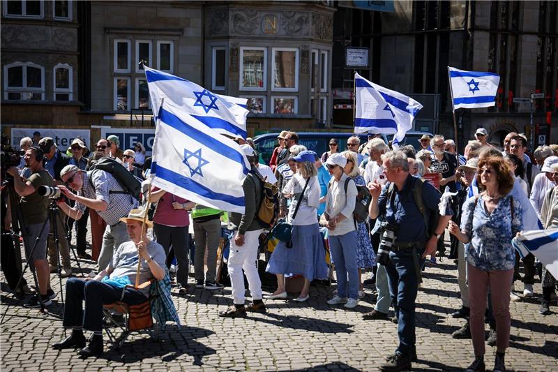 Teilnehmer einer Kundgebung der deutsch-israelischen Gesellschaft Bremen/Unterweser zum Unabhängigkeitstag des Staates Israel stehen mit israelischen Flaggen auf dem Marktplatz in Bremen.