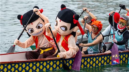 Teilnehmer in bunten Kostümen rudern beim Drachenbootfest in Hongkong.