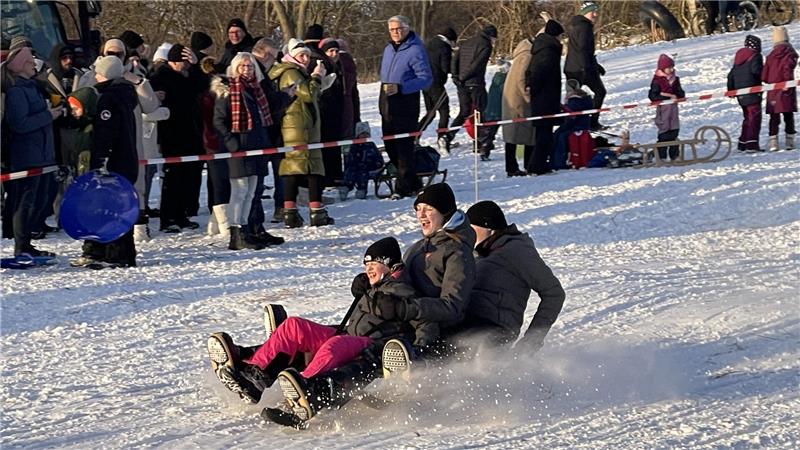 Drei Personen rodeln auf einem Schlitten.
