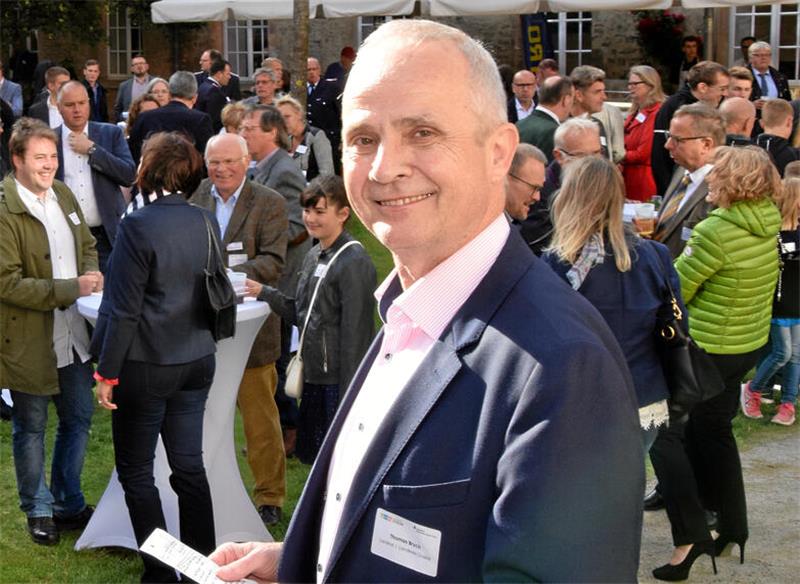 Gruppe von Menschen in einem Außenbereich bei einer Veranstaltung, viele tragen Namensschilder und unterhalten sich stehend.