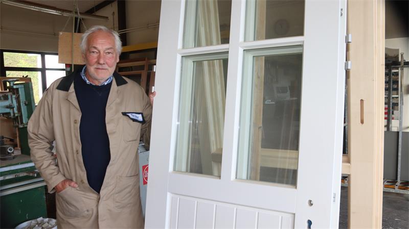 Ein Mann steht in einem Kittel an einer Tür.