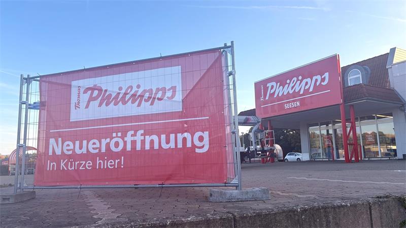 Großes rotes Banner mit weißer Aufschrift 'Philipps Neueröffnung In Kürze hier' vor einem Gebäude mit rotem Schild 'Philipps'