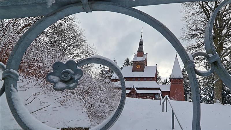 Verschneite Stabkirche hinter einem eisbedeckten schmiedeeisernen Tor mit Blumenornament
