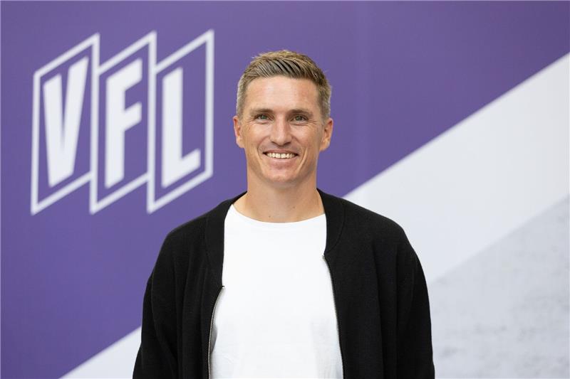 Tobias Schweinsteiger posiert vor einem Vereinslogo im Stadion an der Bremer Brücke.