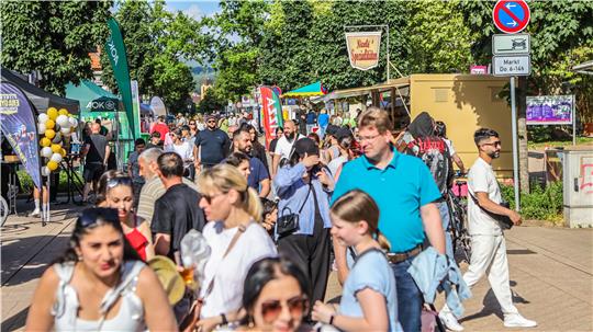 Menschenmenge auf einem belebten Straßenfest mit Ständen, Ballons und Sonnenschein