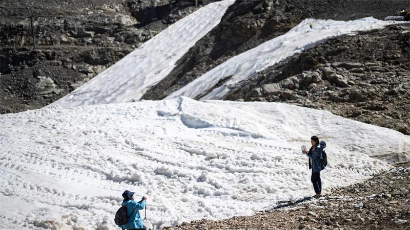 Touristen fotografieren in den Schweizer Alpen Schneereste an einer Skipiste. 