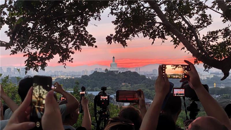 Touristen fotografieren mit ihren Handys den farbenfrohen Sonnenuntergang über der chinesischen Hauptstadt.