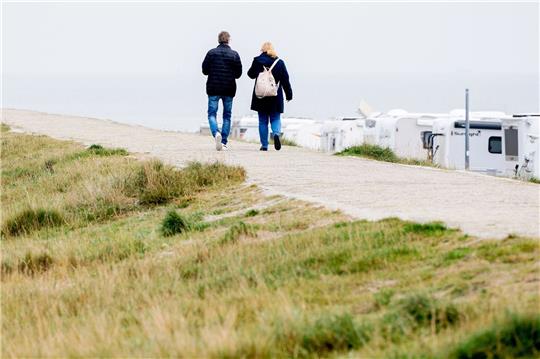 Touristen gehen bei trübem Wetter auf einem Deich vor der Nordsee entlang.
