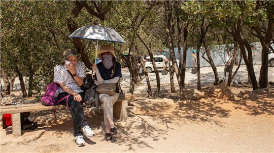 Touristen sitzen unter Bäumen am Eingang der Akropolis in Athen.