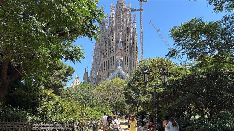 Touristen suchen bei großer Hitze den Schatten auf der Placa de la Sagrada Familia vor der gleichnamigen Basilika in Barcelona. (Archivbild)