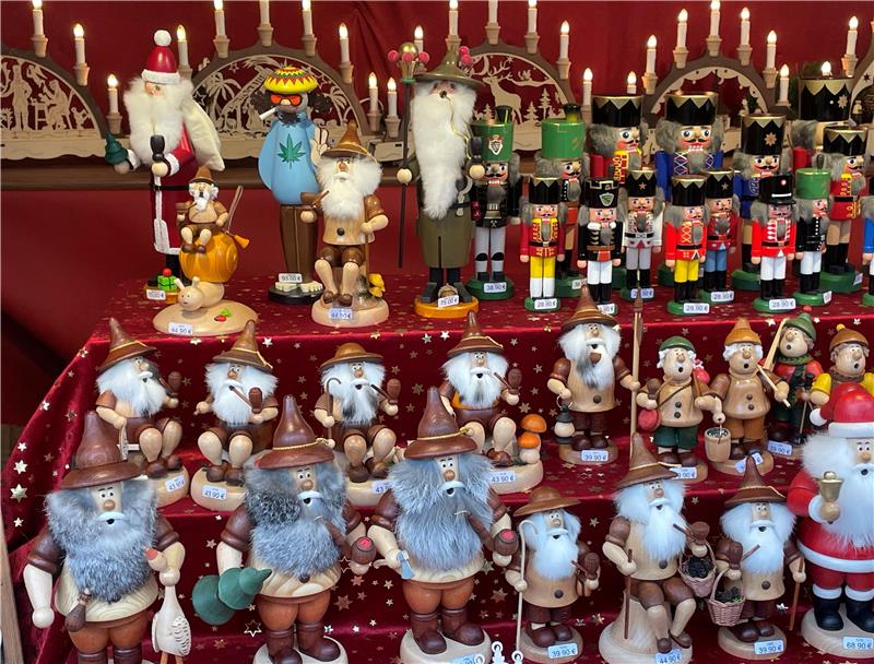 Heiße Geschenktipps: Kleine weißbärtige Rotnasen aus Sachsen Mehrere Reihen von traditionellen Räuchermännchen in verschiedenen Größen und Farben, darunter Figuren mit langen Bärten, Hüten und Weihnachtsmützen, auf einem roten Tuch mit Sternenmuster.