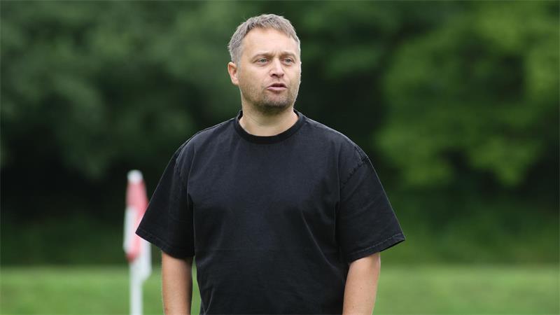 Mann mit schwarzem T-Shirt und Armbanduhr steht auf einer Wiese vor unscharfem grünem Hintergrund