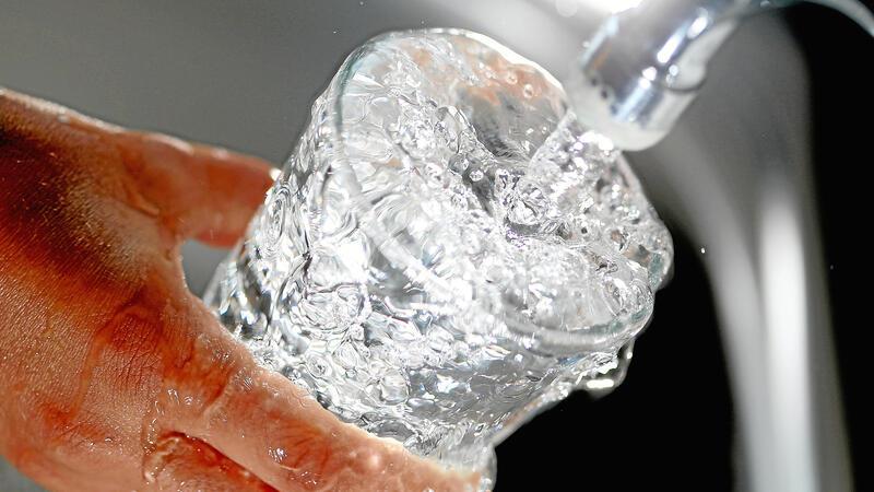 Eine Hand hält ein Glas unter einen laufenden Wasserhahn.