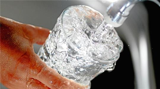 Eine Hand hält ein Glas unter einen laufenden Wasserhahn.