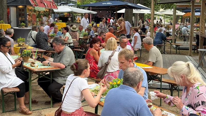 Das Foto zeigt vollbesetzte Tische und Bänke in einem Park.