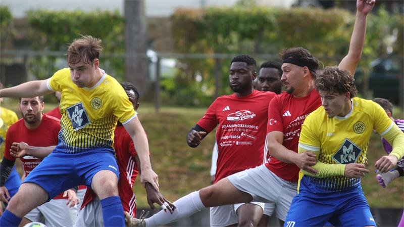Fußballspiel mit mehreren Spielern in gelben und roten Trikots, zwei Spieler in gelben Trikots springen und treten nach dem Ball