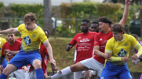 Fußballspiel mit mehreren Spielern in gelben und roten Trikots, zwei Spieler in gelben Trikots springen und treten nach dem Ball