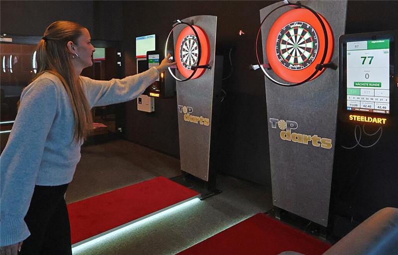 Frau wirft Dartpfeil auf elektronische Dartscheibe in Innenraum mit zwei Dartscheiben und digitaler Anzeige