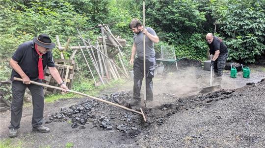 Udo Paul (r.) und seine Köhlergesellen trennen die Kohle von der feinen Erde des Meilers.