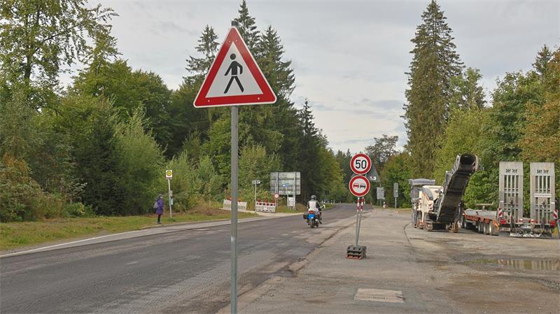 Straße mit Fußgänger-Warnschild, Geschwindigkeitsbegrenzungsschild 50 km/h, Motorradfahrer und Lkw auf der rechten Seite
