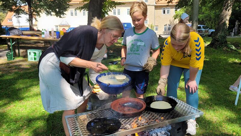 Über einer Feuerstelle bereitet Elisabeth Sielaff mit den Kindern Pfannkuchen zu.