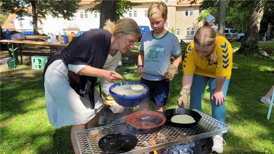 Über einer Feuerstelle bereitet Elisabeth Sielaff mit den Kindern Pfannkuchen zu.
