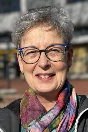 Postbank-Schließung: Das sagen Kunden, die FDP will eine Petition Frau mit kurzen grauen Haaren, die ein bunt gemustertes Halstuch und eine schwarze Jacke trägt