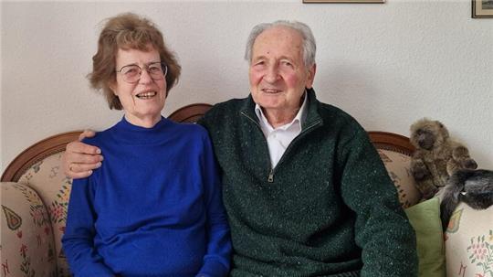 Älteres Paar sitzt auf einem Sofa, der Mann hat seinen Arm um die Frau gelegt.