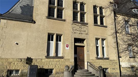 Fassade eines historischen Gebäudes mit mehreren Fenstern, einer steinernen Treppe und einem Schild neben der Eingangstür.