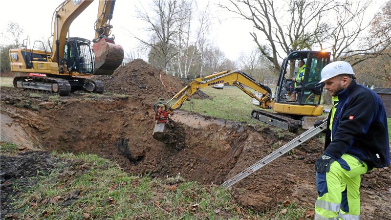 Wasserversorgung in Liebenburg: Wie die Gemeinde sich Hilfe holt Ein Bagger schrabt mit seiner Schaufel an der Wand eines Loches entlang, ein Arbeiter steht im Vordergrund.
